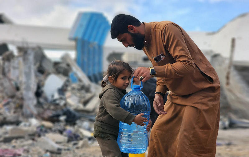 Мужчина помогает ребенку нести емкость с водой